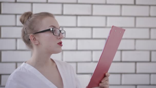 Retrato de mujer de oficina en gafas con camisa blanca y labios rojos sosteniendo carpeta con papeles y documentos de lectura aislados sobre fondo blanco — Vídeos de Stock