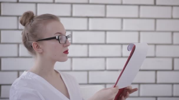 Retrato de mujer de oficina en gafas con camisa blanca y labios rojos sosteniendo carpeta con papeles y documentos de lectura aislados sobre fondo blanco — Vídeos de Stock