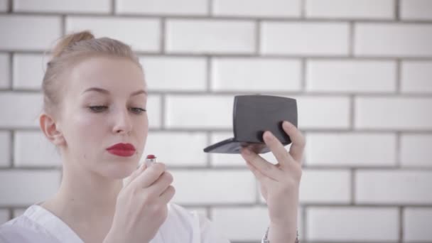 Ung vacker kvinna, målar läppar med rött läppstift, vit bakgrund. — Stockvideo