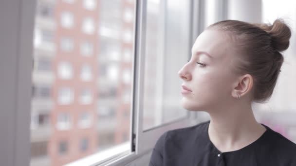 Fundersam kvinnans profil tittar ut genom fönstret — Stockvideo
