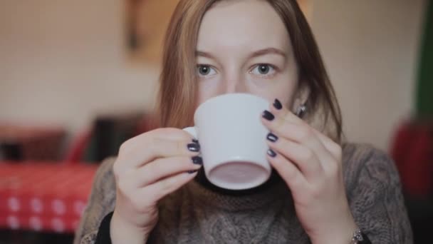 女性は、コーヒーを飲みます。カフェでカメラに笑顔若い魅力的な女性。幸せな女の子のカフェでのんびりとコーヒーを飲んで笑顔でカメラ目線します。一杯のコーヒーと美しい女性 — ストック動画