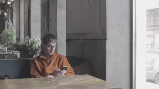 Giovane, triste uomo con il telefono in attesa di qualcuno nel caffè della città — Video Stock