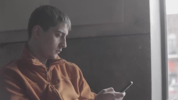 Pencere kafede oturan smartphone kullanan genç adam — Stok video