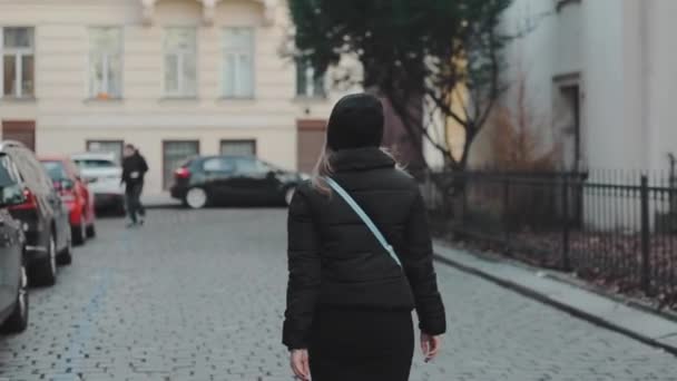 Молодая привлекательная туристка в черной одежде ходит по старому городу. Молодые туристки смотрят на следы в Европе — стоковое видео