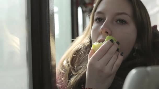 Девушка смотрит в окно автобуса и съедает яблоко днем. Женщина смотрит в окно автобуса днем во время путешествия — стоковое видео
