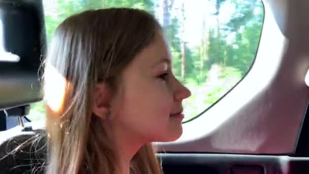 Милая маленькая девочка едет в машине на заднем сиденье и выглядит счастливой . — стоковое видео