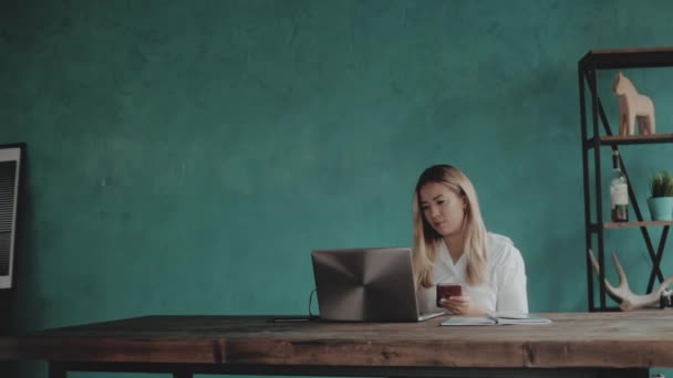 Jonge mooie zakenvrouw zitten aan een tafel met een laptop in haar handen. — Stockvideo