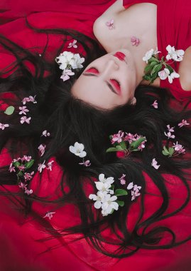 Genç Sevimli Asya modeli ve kadın ile çiçeği çiçek saç modeli mükemmel makyaj. Kapalı gözlü güzel kız kırmızı elbise parçası üzerinde dinleniyor