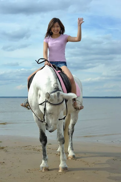 Young asian woman riding white horse on the beach