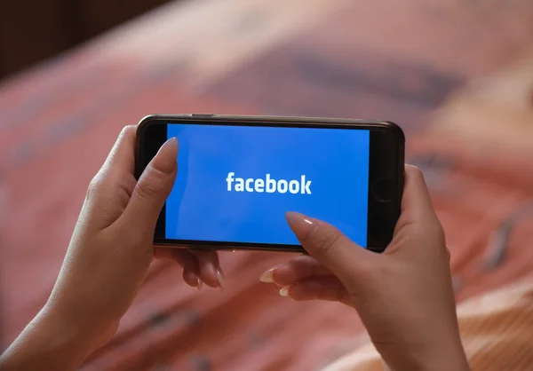 Женская рука с маникюром держа сотовый телефон с Facebook — стоковое фото