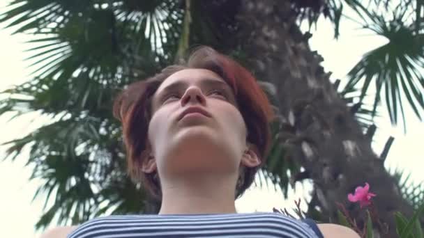 Young woman standing on embankment under palm tree — Stockvideo