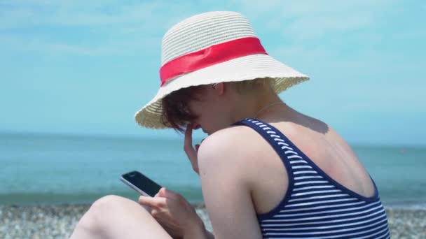 Vista de cerca de la mujer joven utilizando el teléfono inteligente en la mano en la orilla del mar fondo abstracto — Vídeos de Stock