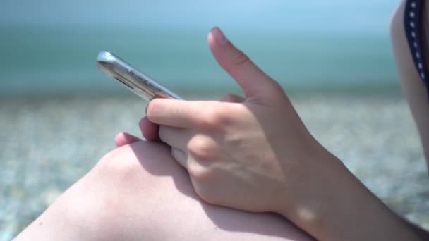 Primer plano de la mano de la mujer joven utilizando el teléfono inteligente en la orilla del mar fondo abstracto. Concepto de descanso y tecnología . — Vídeos de Stock