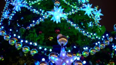 Çok renkli çelenkler, toplar ve yıldızlarla süslenmiş meydanda yakın plan Noel ağacı