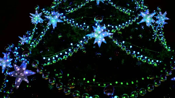 Cidade magnífica Árvore de Natal em quadrado brilhando com luzes verdes, azuis e amarelas de guirlandas, bolas e estrelas — Fotografia de Stock