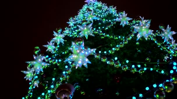 Gros plan grandes étoiles bleues multi-pointes lumineuses et décoration boules jaunes sur le sapin de Noël sur la place du marché de Noël — Video