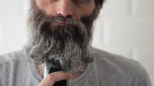 Dlouhé pološedé vousy muž středního věku se snaží oholit s elektrickým střihačem vlasů — Stock video