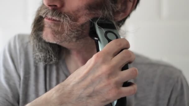 Medelålders man klipper kvarvarande ansiktshår efter rakning av långt halvgrått skägg — Stockvideo