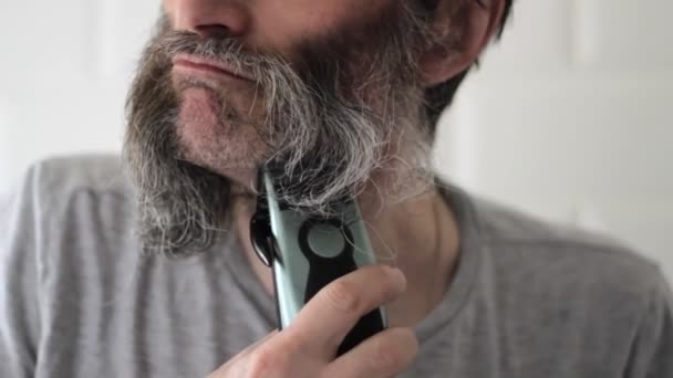 Muž středního věku stříhá dlouhé pološedé vousy a knír elektrickým střihačem vlasů — Stock video