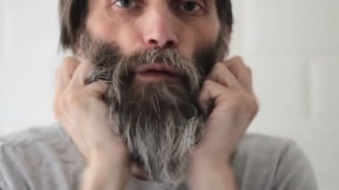 Uzun, yarı gri sakallı, orta yaşlı, sakallı bir adam.