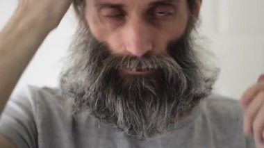 Orta yaşlı adam sakalı elleriyle, tarağı da pembe tarağıyla temizler.