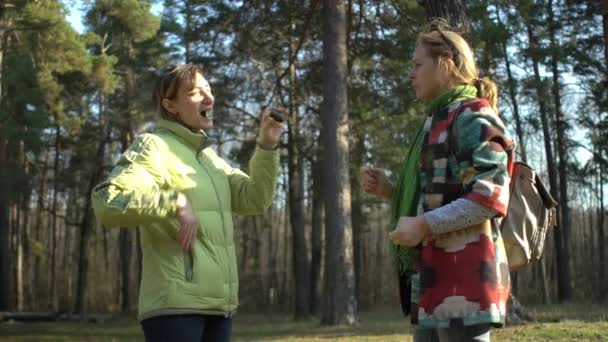 Kaksi keski-ikäistä naista syömässä kurkkua metsäaukiolla. — kuvapankkivideo