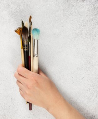 Gri taştan arka planda dişi bir elde sanatsal fırçalar..