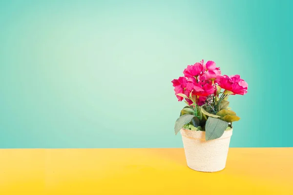 Artificial flower pot over yellow floor with green smooth background and vintage styl tone.