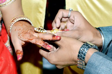 Indian groom putting wedding ring on bride's hand clipart