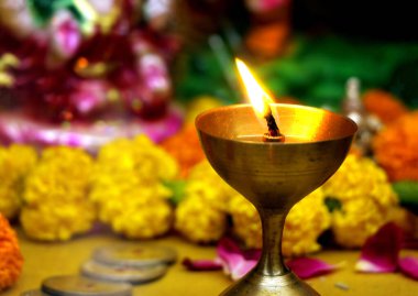 Marigold çiçekleri, gül yaprakları ve tapınma eşyalarıyla çevrili, parlak bir alevle aydınlatılmış bir pirinç yağ lambası (diya) yakın çekimi