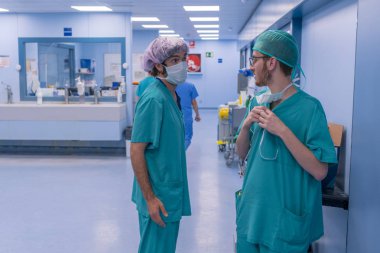 İki cerrahlar O.R. konuşurken önce koğuşta. Bir maske ile pembe şapka takıyor ve diğer yarı-maske ile yeşil bir şapka giyer.