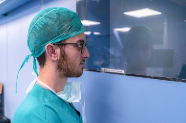 Tıp öğrencisi bir O.R. camdan bakıyor. Sakal ve gözlük ile cerrahi şapkasını genç dostum ve maskesini laubali