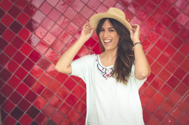 Kız bir şapka kırmızı bir duvar önünde poz. O şapka onun elinde. Kırmızı pantolon ve beyaz tişört giyiyor. Sağdaki alan içeren yatay fotoğraf