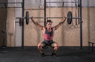 Spor salonunda ağırlık kaldırma çubuk güçlü genç adam. Bir tank top ve şort giyiyor. O uzun saçlı.