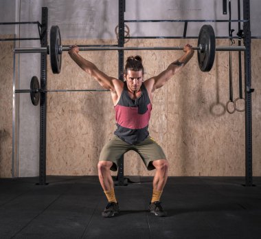 Spor salonunda ağırlık kaldırma çubuk güçlü genç adam. Bir tank top ve şort giyiyor. O uzun saçlı.