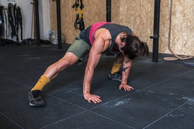 Yapan güçlü genç erkek spor salonunda uzanır. Tek bacaklı uzanmış yere bakıyor. Uzun saçlı
