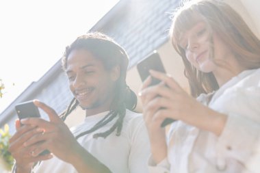 Afro erkek ve kızıl saçlı beyaz kız terasta cep telefonu yla sohbet ediyor. Güneşli bir gün. Resim aşağıdan