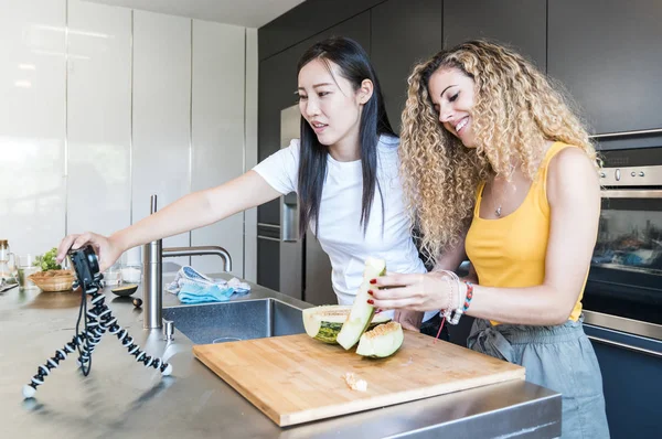 Caucasian girl and Asian girl young cutting fruit in a modern ki