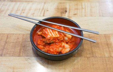 Ahşap bir masa üzerinde bir kil plaka ve metal çubuklar Kore kimchi.