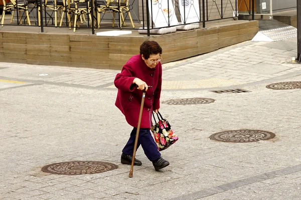 Una mujer de ochenta años con un palo cruza la calle . — Foto de Stock