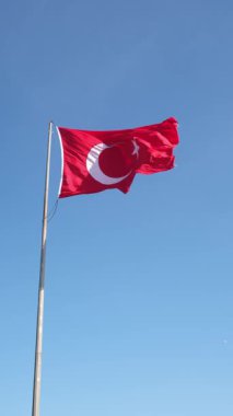 Kırmızı hilal ve yıldızlı Türk bayrağı, açık mavi gökyüzü arka planında gururla dalgalanırken, vatanseverlik gösterisinde Türkiye 'nin ulusal sembolünü gösteriyor