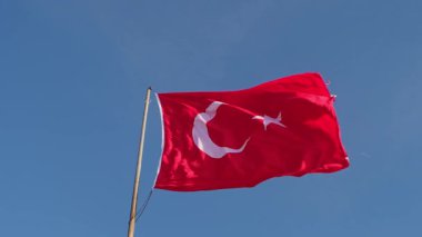 Kırmızı hilal ve yıldızlı Türk bayrağı, açık mavi gökyüzü arka planında gururla dalgalanırken, vatanseverlik gösterisinde Türkiye 'nin ulusal sembolünü gösteriyor