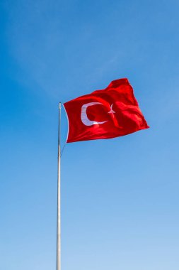Kırmızı hilal ve yıldızlı Türk bayrağı, açık mavi gökyüzü arka planında gururla dalgalanırken, vatanseverlik gösterisinde Türkiye 'nin ulusal sembolünü gösteriyor