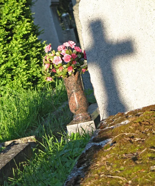 Skugga av argt på tombstenen, grav med konstgjorda blommor Stockbild