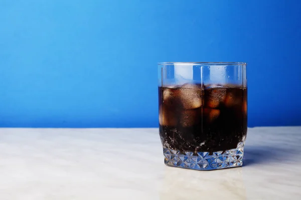 Glass of cola with ice on the bar, blue background, place for your text.