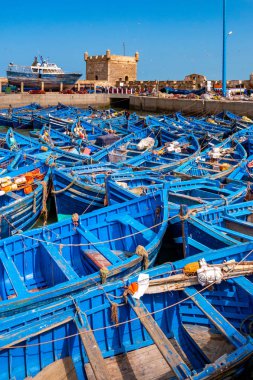 Mavi balıkçı tekneleri filosu birlikte bağlantı noktası Essaouira Fas'ta huddled. Ayrıca sur duvarları ve Mogador kalesinin Kulesi görebilirsiniz