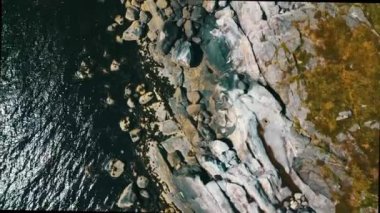 Kayalık bir kıyı üzerinde uçmak, yukarıdan dikey manzara, temiz, şeffaf su, Norveç 2020 (4K). Güneşli bir yaz gününde çekilmiş. Kullanılan nötr filtre ND32.