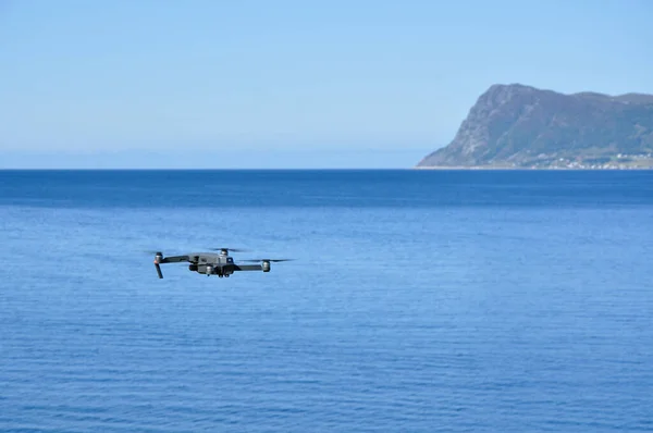 Arkasında dağlar ve deniz olan bir dron havada uçuyor..