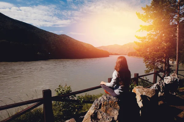girl is engaged in meditation and yoga with a view of mountains and river, toned photo, glare of the sun, blue sky. Concept freedom, travel, vacation from city.