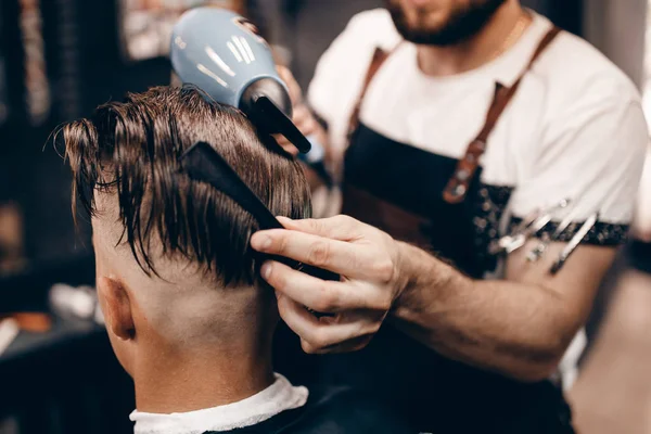 一个年轻的时髦家伙在理发店理发剪和打字机 打蜡头发 吹干头发的特写 概念男装的地方 色调的照片 软焦点 — 图库照片
